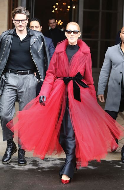 Céline con uno de sus looks más llamativos en París: vestido negro de cuero con cuello Perkins y abrigo rojo de tul con cinturón de terciopelo negro, de Óscar de La Renta. Detrás, su inseparable amigo Pepe Muñoz