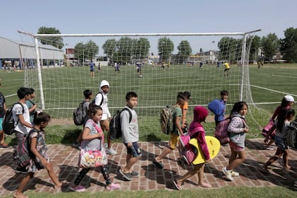 Los chicos de la colonia cruzan el camino que pasa por detrás de la cancha de césped sintético donde entrenan los jugadores