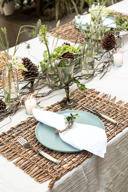 Centro de mesa con ramas, piñas y floreros con flores frescas.