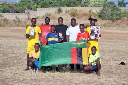 Chicos de la ONG en Zambia sostienen la bandera del país junto a un muñeco y dos imágenes de Diego Maradona