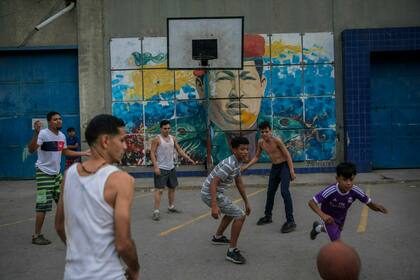 Chicos juegan al basquetbol con un mural del difunto presidente de Venezuela, Hugo Chávez, en el fondo, en Caracas