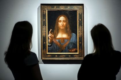 Christies employees pose in front of a painting entitled Salvator Mundi by Italian polymath Leonardo da Vinci at a photocall at Christies auction house in central London on October 22, 2017 ahead of its sale at Christies New York on November 15, 2017. Salvator Mundi, one of fewer than 20 known paint