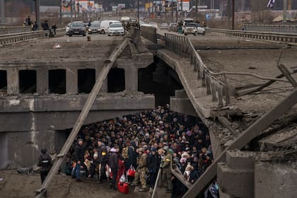 Cientos de ucranianos intentan cruzar debajo de un puente destruido cruzando el río Irpin en las afueras de Kiev, Ucrania, el 5 de marzo de 2022.