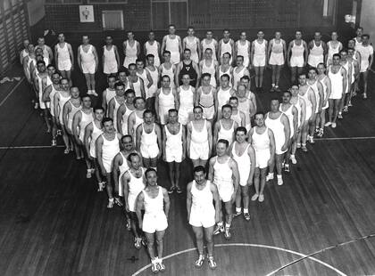 Clase de gimnasia de la Asociación Cristiana de Jóvenes (YMCA). Los alumnos forman un triángulo, emblema de la institución.