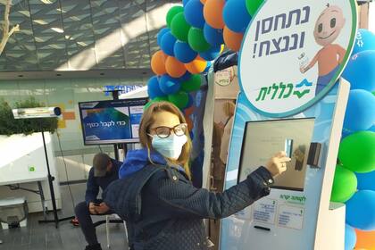 Claudia Oppenheimer registrándose con su carnet de obra social en el centro de vacunación: el cartel dice "nos vacunaremos y venceremos"