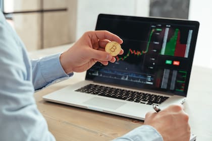 Closeup view picture with no face of male trader investor holding bitcoin, using laptop with diagram of trading stock market, investing in cryptocurrency at his office. Investment and technology