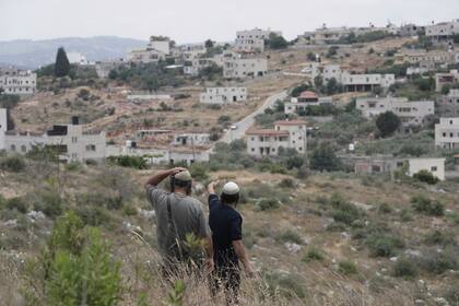 Colonos israelíes miran hacia un pueblo vecino en Cisjordania