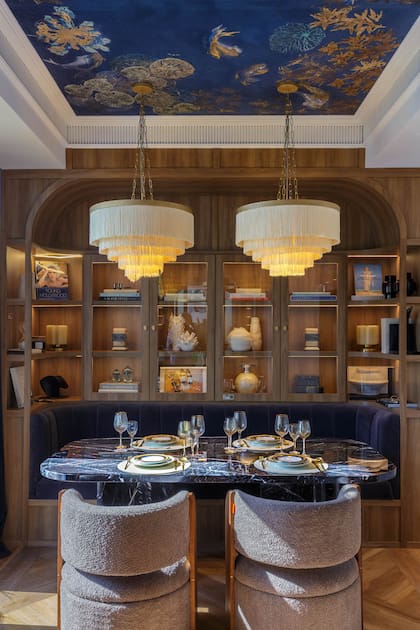 como respaldo de la mesa de mármol ‘Negro Marquina’ (RAV Estudio), una biblioteca hecha a medida que contiene un asiento tapizado en terciopelo (todo de C’est Moi). Vajilla (Deco Vintage New). Obra "Hombre en Milán", de Daniel Karp (Diderot.art).