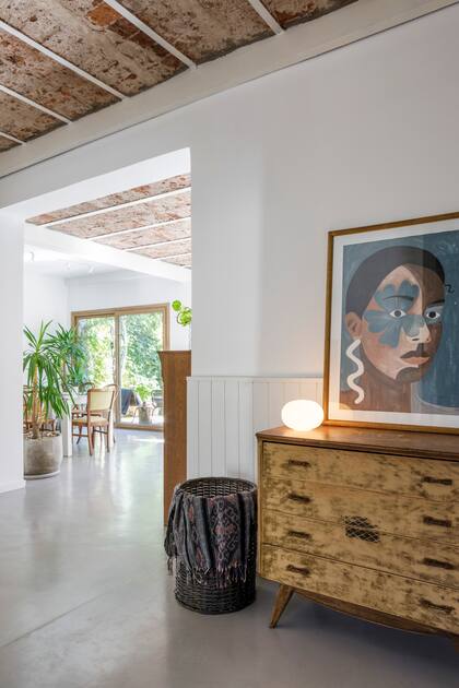 Cómoda heredada y restaurada, cuadro pintado por la dueña de casa, canasto encontrado en la calle. “Además de ser una solución rápida para prevenir humedades desde el jardín vecino, poner una placa cementicia y revestirla con machimbre pintado le dio onda al espacio, que quedaba muy grande y vacío visualmente”, dicen.