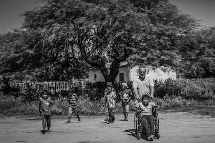 El sacerdote Juani Rosasco lleva a Benjamín en su silla de ruedas, en la comunidad rural de Tres Pozos