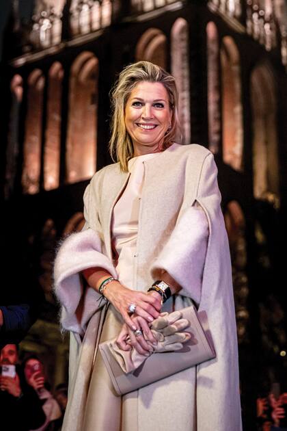 Con clutch Hermès, guantes de cuero, destacados anillos en ambas manos y su reloj Cartier, Máxima posa con la torre iluminada como telón de fondo.
