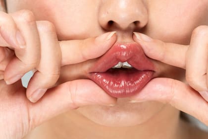 Con el pulgar y el índice formar una pinza y tomar el labio inferior, como si uno fuera a preparar la boca para chiflar