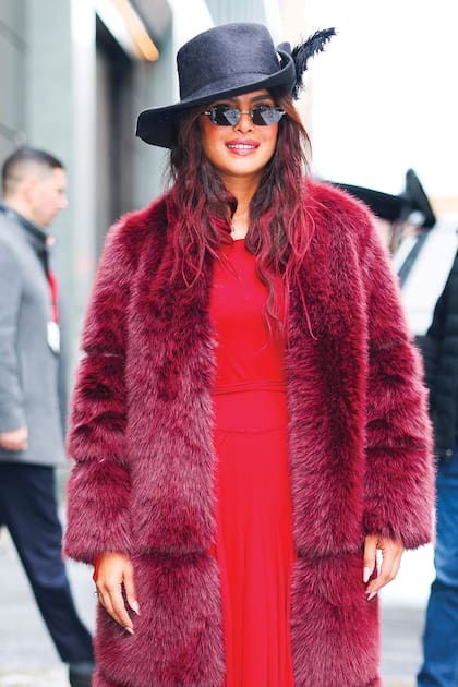 Convirtiuna fra maana de NuevaYork en un momento demoda con un abrigo de pielen capas sobre un vestidorojo, sombrero con plumas yanteojos oscuros