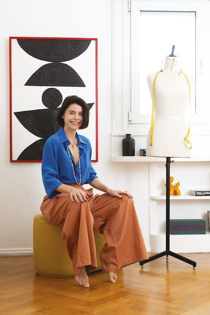 Corine Fonrouge en su estudio, sobre puf de Pastel y junto a una obra de arte de Mariana Ayraudo