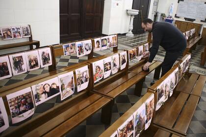 El padre del sacerdote católico Georges Nicoli pega las fotos de los fieles en los bancos de la iglesia antes de dar la misa de Pascua
