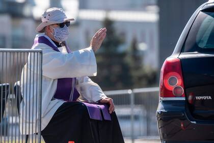 Un sacerdote con una máscara facial confiesa a un creyente en un estacionamiento frente al Templo de la Divina Providencia de Varsovia, Polonia