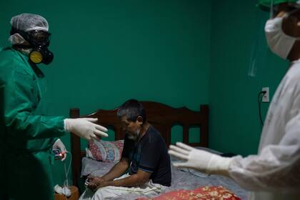 Plinio dos Santos, de 65 años, que tenía dificultades para respirar, se sienta en su cama mientras el trabajador de emergencias verifican su nivel de saturación de oxígeno antes de transferirlo a un hospital donde posteriormente fue admitido sospechoso de tener COVID-19