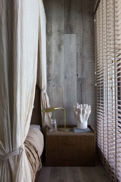 Cortinas roller en madera (Hunter Douglas by Arteplano). Las mesas de luz (Wood Market) tienen una delicada unión de madera y rafia, material que aparece también en el respaldo de cama.