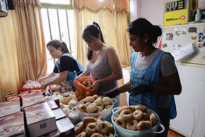 Cristina, junto a Johana y Natalia, preparan las rosquitas, el pan casero y la mercadería que van a repartir a las familias que esperan junto a la puerta de su departamento, que es también la sede del merendero "El Fuerte"

