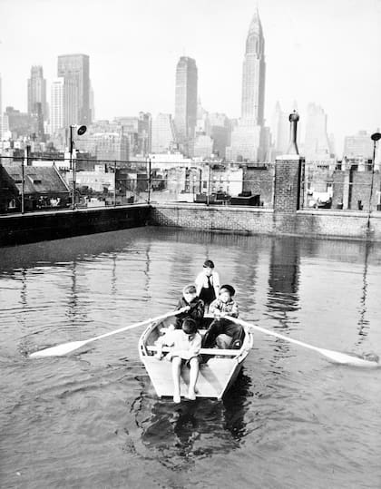 Cuatro niños, miembros del Madison Square Boys Club, reman en un bote de remos en una piscina en la terraza con Manhattan a lo lejos, en Nueva York, en febrero de 1950.