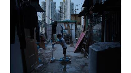 Un niño de cinco años juega fuera de su pequeña casa hecha de hormigón y de chapa en la terraza de un bloque de departamentos.