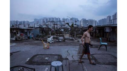 Un residente camina fuera de su choza ilegal en la terraza situado al lado de una residencia estatal pública, en el fondo.