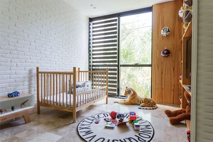 Cuna en madera de lenga (Krethaus). Biblioteca para juguetes y enchapado de pared en madera de paraíso (OON Architecture). Alfombra (Multiply). Cortinas de velo traslúcido y telas horizontales (Hunter Douglas).