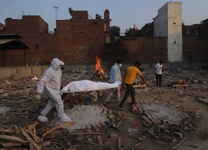 Damiliares y voluntarios cargando el cuerpo de una víctima de COVID-19 para ser incinerada en Nueva Delhi, India