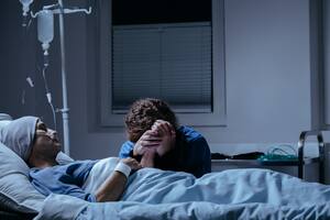 Daughter crying at her dying mother's bed in the hospital. Breast cancer concept