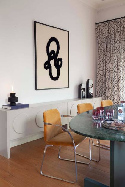 De cara a la chimenea con frente moldurado, cómoda laqueada (Bull Buenos Aires) con círculos en cada puerta, cuadro de Polonio y juego de jarrones de cerámica (Sol Larrosa).