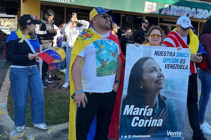 De izquierda a derecha, los venezolanos David Núñez, Lisbeth García y Víctor Giménez se reúnen fuera del restaurante El Arepazo con un cartel de la líder opositora y ganadora del Premio Nobel de la Paz María Corina Machado en las celebraciones por la captura del presidente venezolano Nicolás Maduro en Doral, Florida, el sábado 3 de enero de 2026. (AP Foto/Vanessa Alvarez)