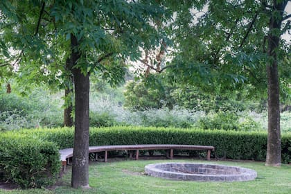 De piedras, abajo de los árboles y protegido por una cortina de buxus que, por cómo fueron situados, acompañan la forma del fogón.