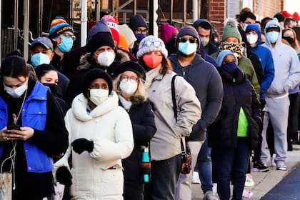 Decenas de residentes de la ciudad hacen una fila que se extiende alrededor de la cuadra para recibir kits gratuitos de prueba rápida de COVID-19 en el hogar, el lunes 20 de diciembre de 2021 en Filadelfia.  La explosión actual de infecciones de coronavirus causada por la variante ómicron en Estados Unidos está causando un colapso de funciones y servicios básicos _ en la última ilustración de cómo el coronavirus sigue trastornando la vida más de dos años después del inicio de la pandemia.(AP Foto/Matt Rourke)