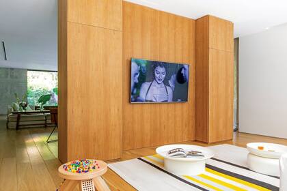 Del otro lado del comedor, el tabique se convierte en un mueble de petiribí que suma espacio de guardado y da soporte al televisor. Organizado sobre la alfombra ‘Horizon’ (Woodnotes), este sector funciona como un living más íntimo y familiar.