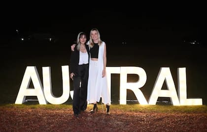 Delfina Lanusse y Chantal Leclercq posan juntas al aire libre, de noche, frente a un cartel luminoso de la Universidad Austral donde estudiaron juntas y se hicieron amigas íntimas