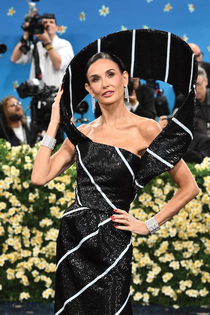 Demi Moore deslumbró con un diseño de Thom Browne de tejido metalizado en
binomio blanco y negro con cola rectangular y una estructura aérea en forma de halo que enmarca
su cara. Lo combinó con brazaletes, anillos y pendientes de diamantes de Shiphra.