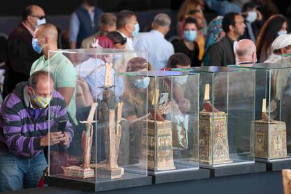 Turistas observan las estatuas y máscaras funerarias encontradas junto a los sarcófagos