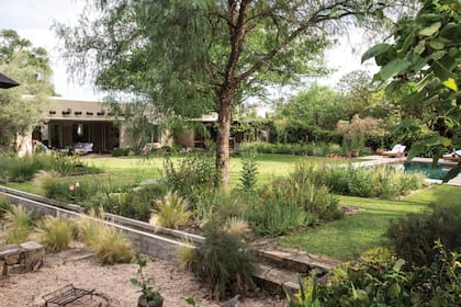 Desde la acequia hacia arriba, aparece la superficie de césped y una plantación más verde, con mayores requerimientos de agua. Del otro lado de la acequia, el xeriscape, con granza cordobesa que cubre la superficie y plantas que van semillando solas.