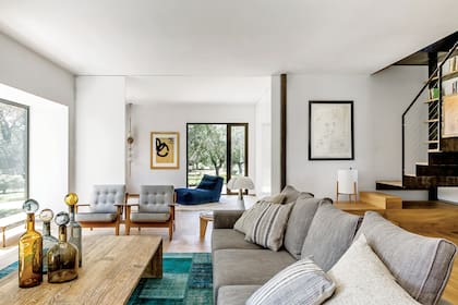 Sofá (Verzelloni), mesa de teca y botellas de cristal (todo de Batavia). Dúo de sillones firmados por Hans Wegner en los 50.