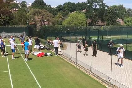 Djokovic (remera blanca, pantalón azul) habla con Kyrgios, que pasa por un pasillo durante un entrenamiento