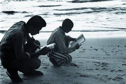 Gaza, 1965. “Dos jóvenes estudian en cuclillas a centímetros del mar, durante el tiempo que les daban en el trabajo para estudiar. La clase se dictaba allí, en la playa, sin mesas ni sillas; es el mismo lugar donde trabajaban y hasta donde muchos de ellos llegaban a pie, descalzos, desde varios kiló