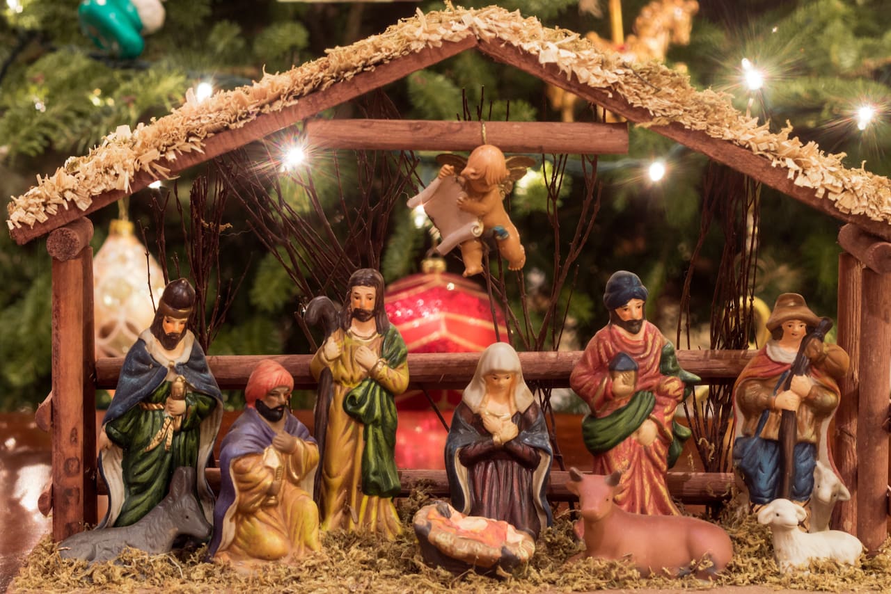Pesebre junto a un árbol de Navidad con luces y figuras del nacimiento