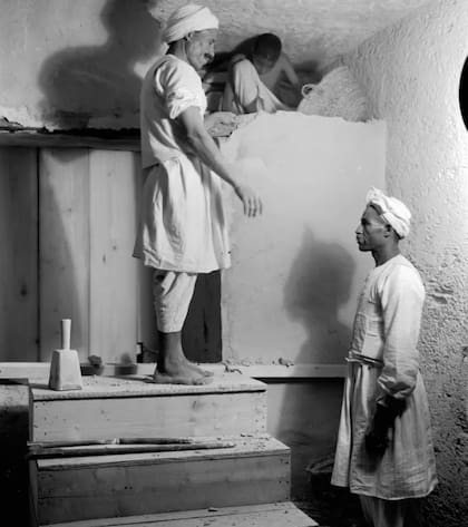 Dos capataces y un niño desmantelando cuidadosamente un tabique para abrir la cámara funeraria