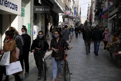 Dos chicas pasean con sus bicicletas usando tapabocas en la calle principal de Atenas, el 6 de abril de 2021