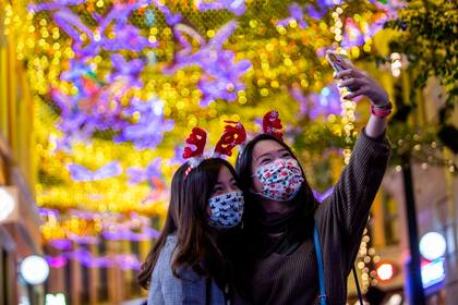 Dos chicas se sacan una selfie portando barbijos con motivos navideños en Hong Kong