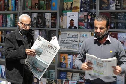 Dos hombres leen periódicos locales con titulares sobre los últimos eventos en su país, frente a un quiosco en la capital