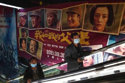 Dos hombres pasan junto al anuncio de una película en Pekín, siempre con barbijo por la suba de casos   