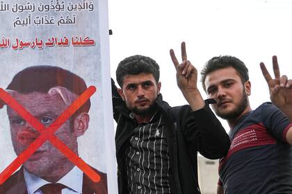 Dos hombres sostienen un letrero que condena al presidente francés Emmanuel Macron, y que lo representa con un hocico de cerdo, por sus comentarios sobre las caricaturas del profeta Mahoma en la ciudad de Idlib, en el noroeste de Siria, el 25 de octubre de 2020