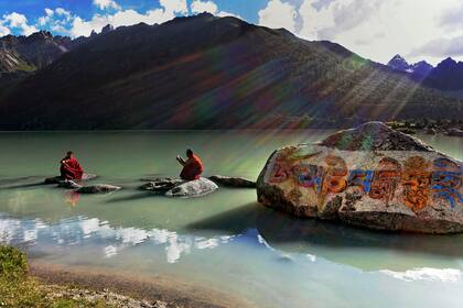 Dos monjes tibetanos en las orillas del lago Yilung Lhatso en el este del Tíbet. El grabado en la roca dice Om Mani Padme Hum, que es el mantra del Buda de la Compasión
