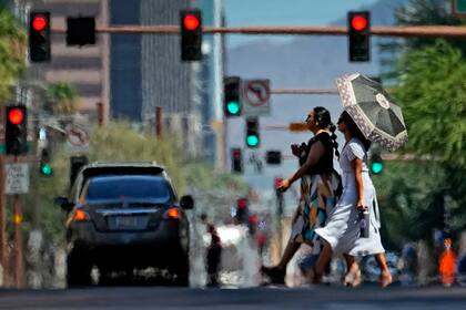 Dos mujeres cruzan la calle en el centro de Phoenix, tratando de esquivar el calor. (AP Foto/Matt York, Archivo)